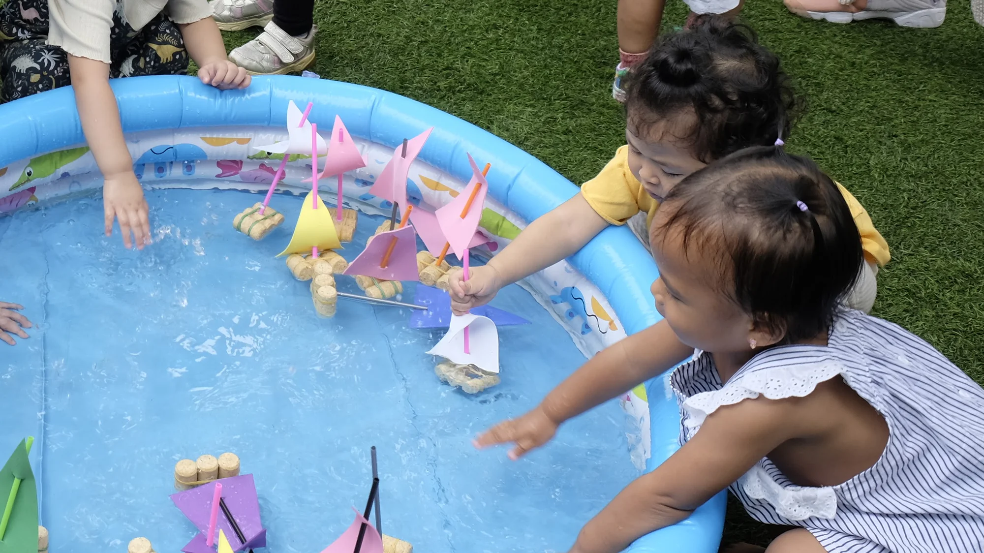 Bayi bermain air dan perahu kertas di kolam kecil