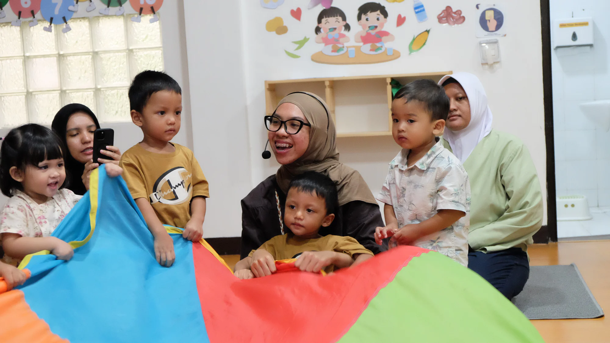 Anak-anak dan pengajar bermain kain parasut di kelas